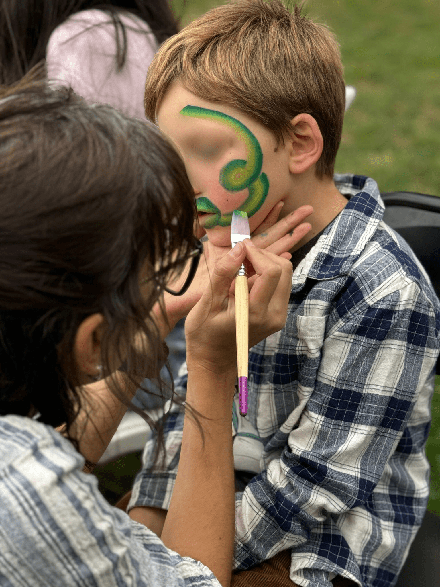 Face painting artist creating a green swirl design on a boy at a party