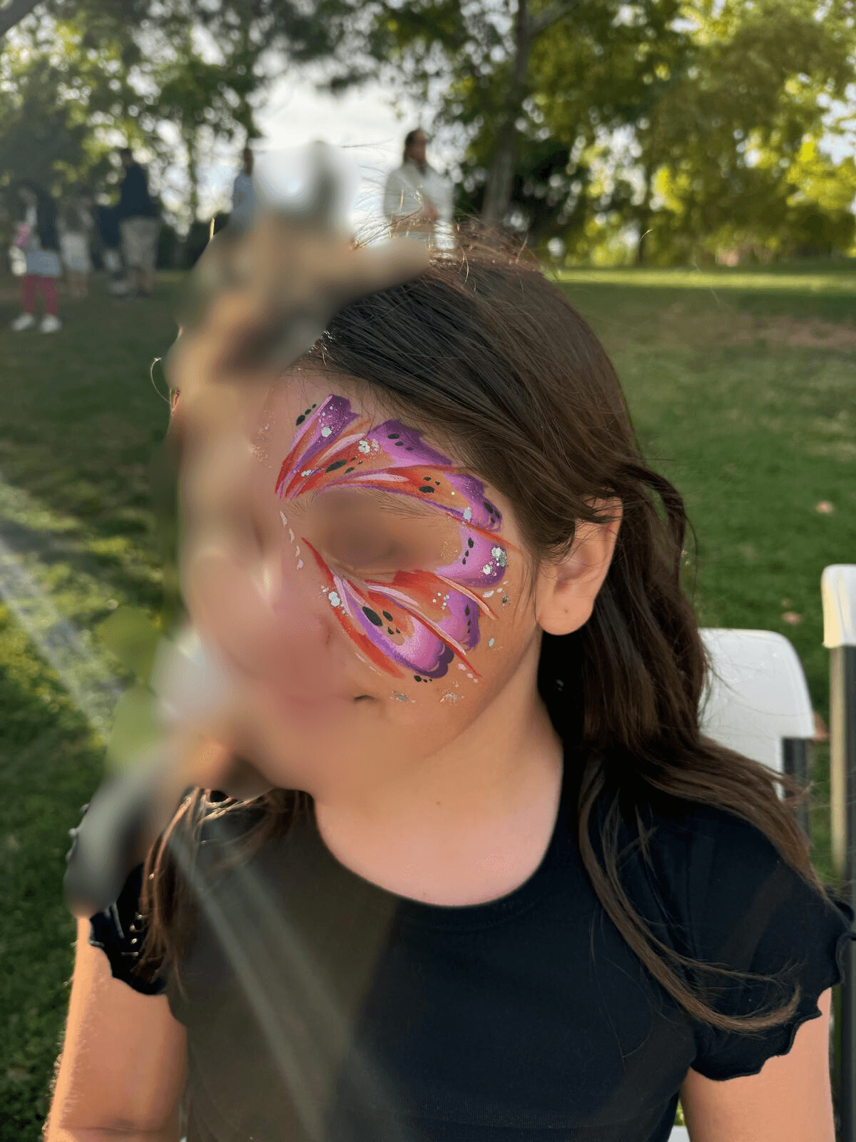 Butterfly face paint with glitter and gems on a girl at an outdoor party